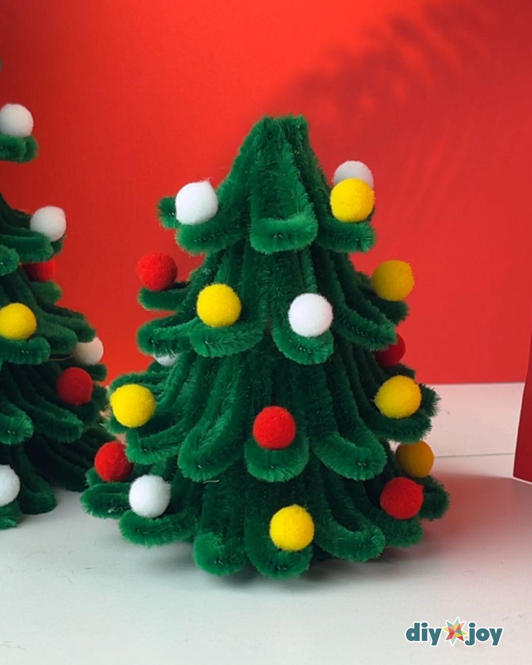 Best DIY Christmas Ideas - a finished mid size pipe cleaner tree covered in red, yellow, and white pom poms on a white table against a red backdrop