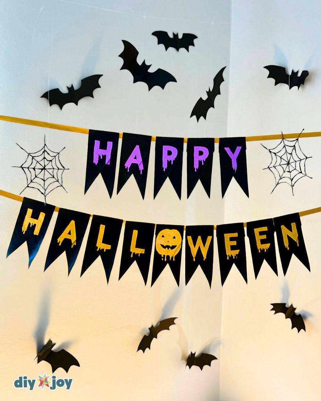 Halloween Crafts - Spooky Toilet Paper Roll Banner spelling Happy Halloween in purple and orange with paper bats.