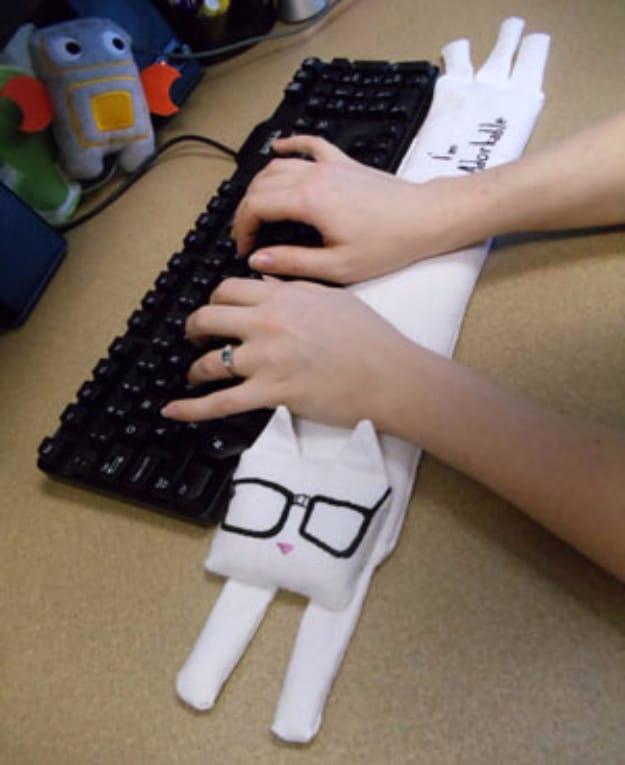 A padded wrist rest sewn to look like a sleeping ginger cat, lying at the front of a keyboard with hands typing