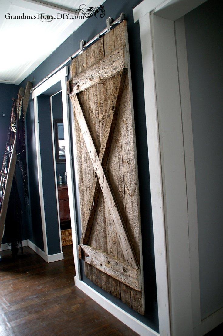 Weathered plank barn door on a metal sliding track across a doorway in a dark blue gray painted room
