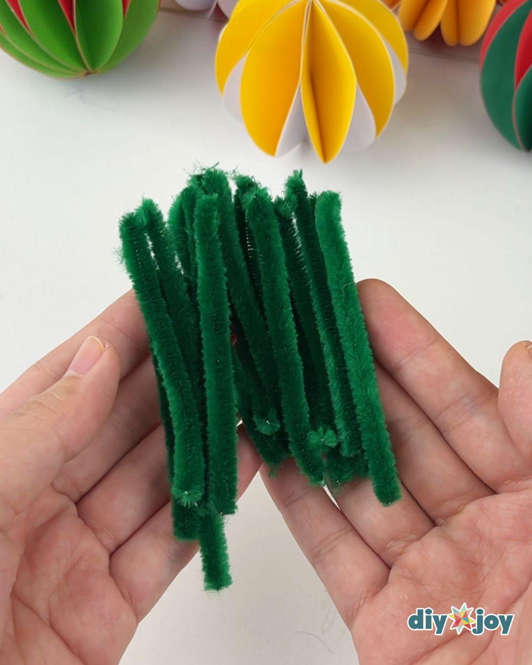 DIY Pipe Cleaner Crafts - two hands hold a bundle of green pipe cleaners that have been folded in half twice over a white table