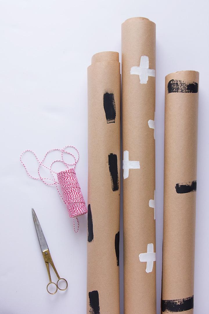Three rolls of kraft paper hand painted with black dashes, white crosses and black blocks beside red twine