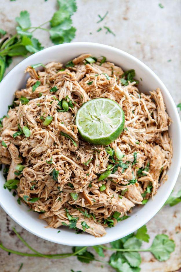 Crock pot Mexican chicken, shredded seasoned chicken in a white bowl with chopped cilantro and a lime half