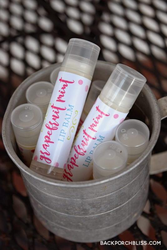 Lip balm tubes with pink grapefruit mint labels standing in a small galvanized bucket on a metal mesh table