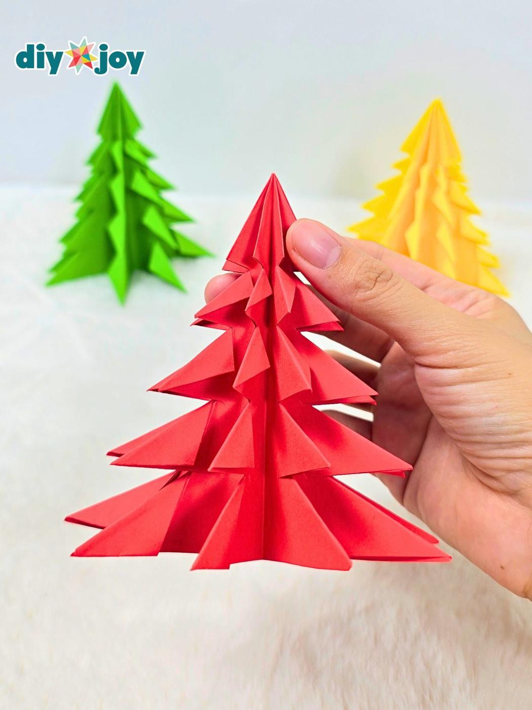Folded origami paper Christmas trees in shades of green and red with fringed tiers standing in a row on a table