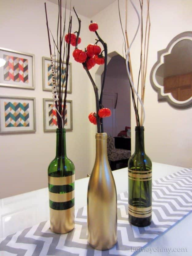 Gold painted wine bottle vases, two green bottles banded in gold beside one sprayed solid gold, holding red berry branches