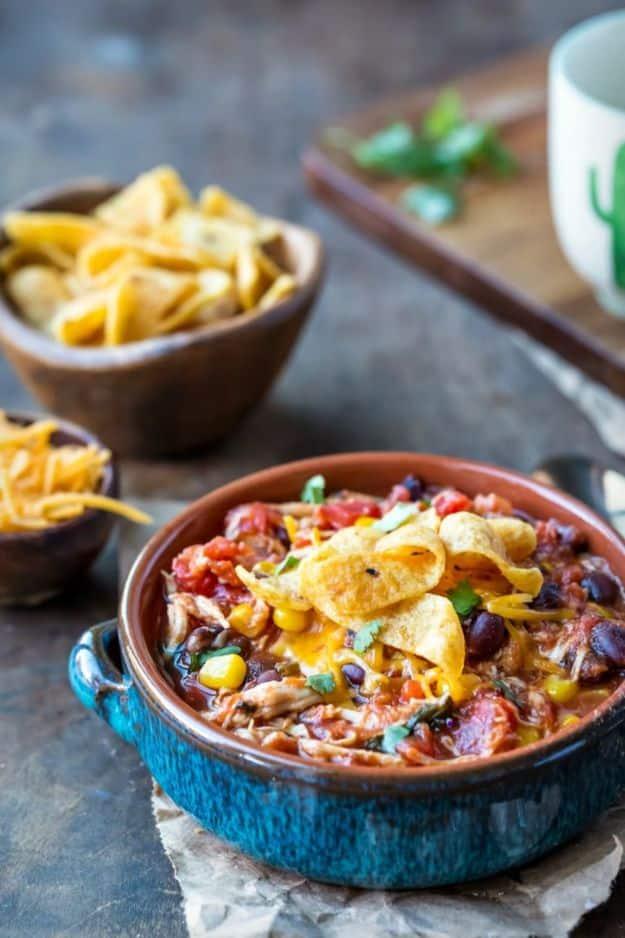 Slow cooker chicken Frito chili in a dark blue two handled bowl with corn chips and shredded cheddar
