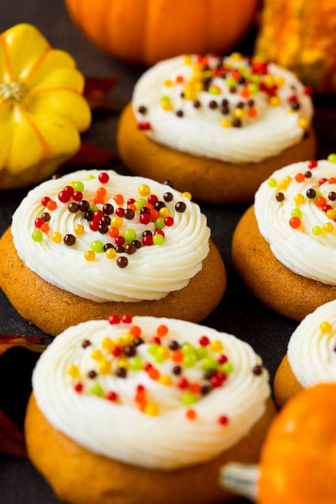 Soft pumpkin cookies topped with piped cream cheese frosting and fall sprinkles beside small pumpkins