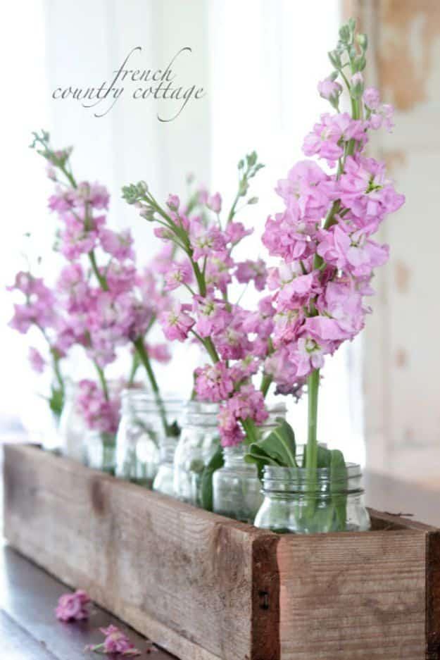 A long wooden box in a soft gray wash sits centered on a dining table, filled with three cream pillar candles