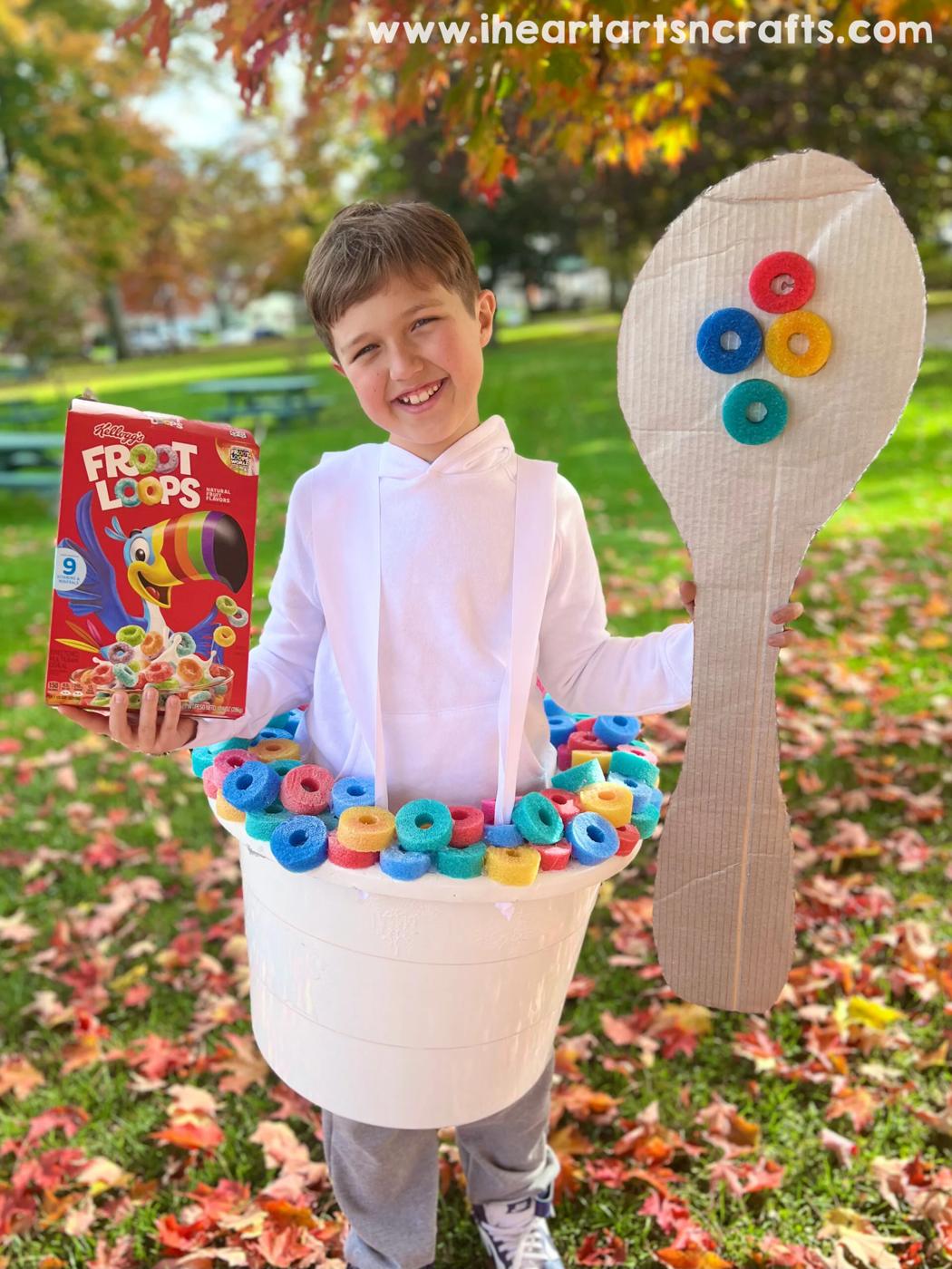 Child wearing a white cereal bowl costume with colorful pool-noodle cereal, cereal box and cardboard spoon outdoors