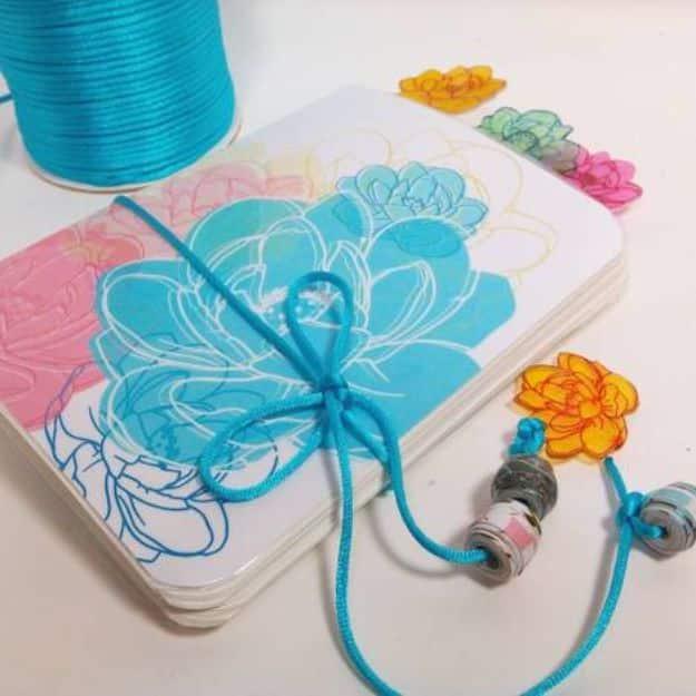 DIY sketchbook journal with a white cover printed in pink, teal, orange and gold outline flowers, tied with a beaded cord
