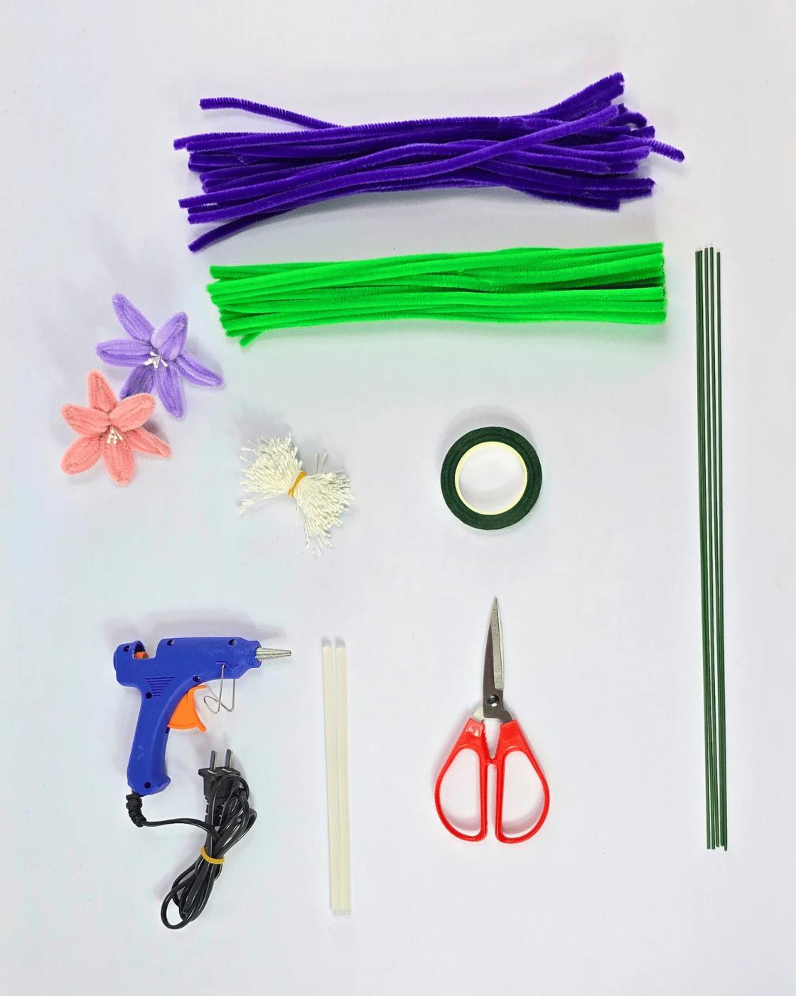 Materials for pipe cleaner lilies laid out on a table, chenille stems in white pink yellow and green