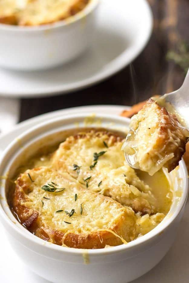 French onion soup in a white crock under browned melted cheese and toasted baguette, thyme scattered on top