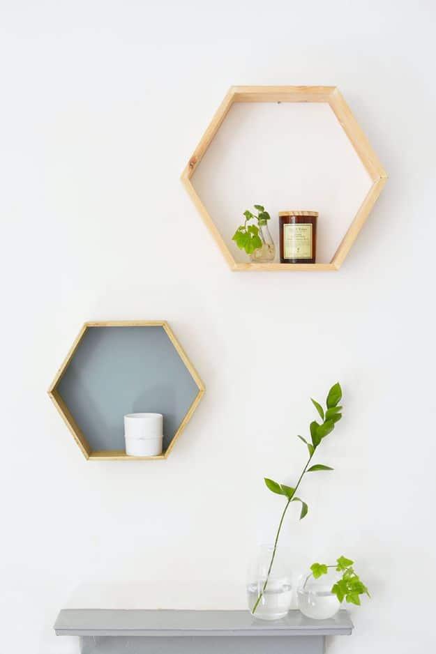 Two wooden hexagon honeycomb shelves on a white wall, one open and one with a grey painted back panel and a candle