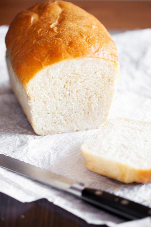 Amish white bread loaf resting on parchment with one soft slice cut from the end and a bread knife alongside