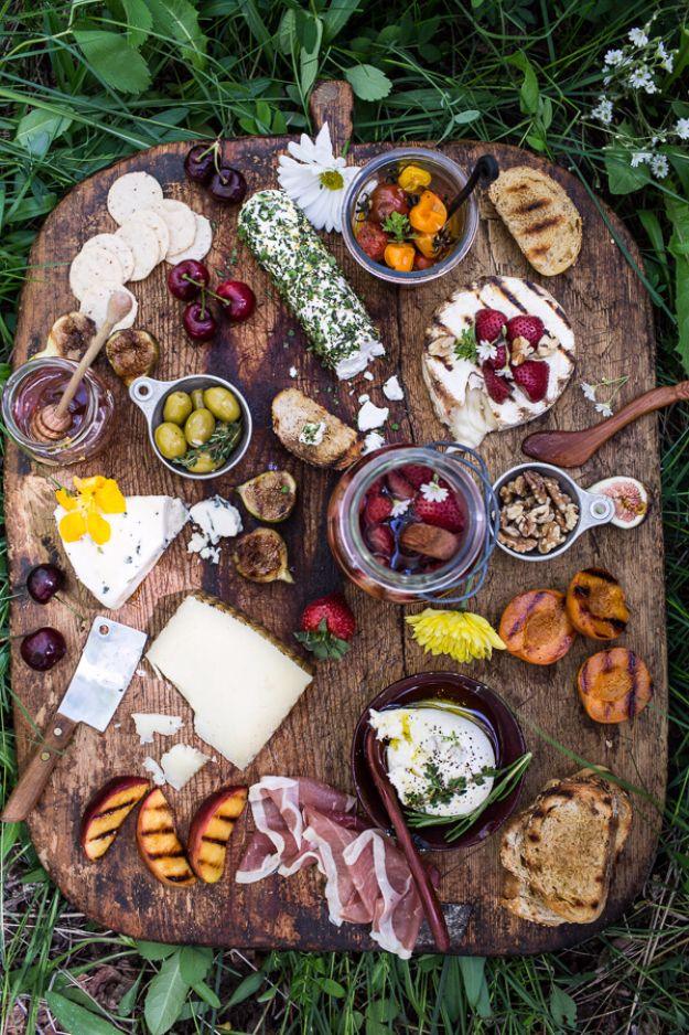 Picnic summer cheeseboard, a rustic wooden board on grass with cheeses, grilled peaches, prosciutto, olives and berries