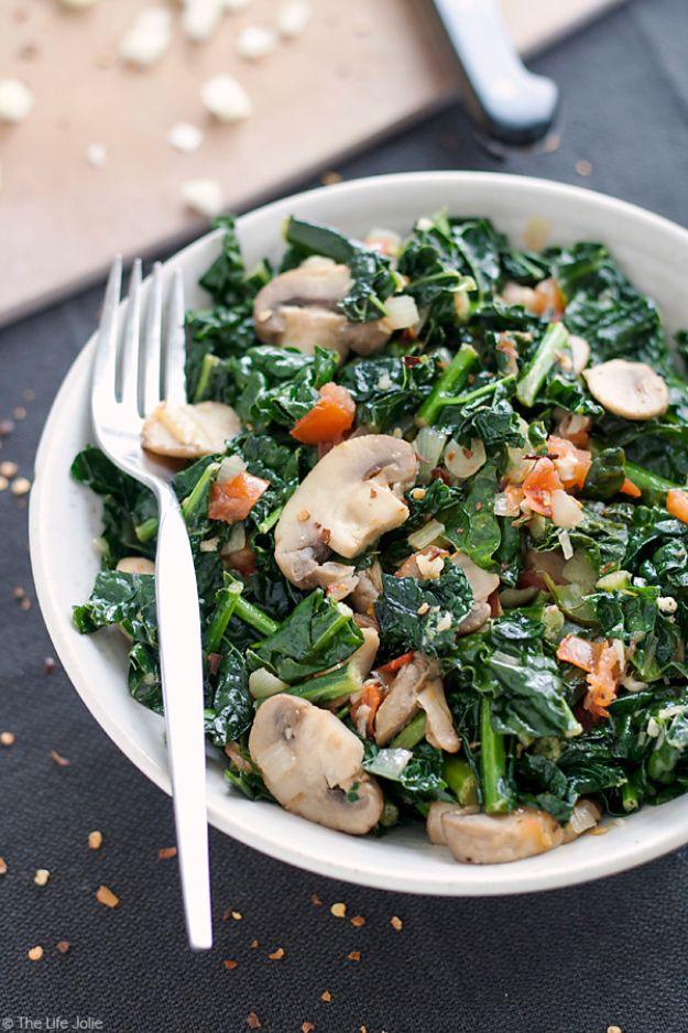 Sauteed kale with sliced mushrooms and diced tomato served on a white plate with a fork on a dark table