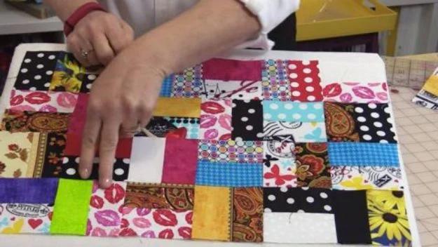 Quilting scraps patchwork quilt top in bright mixed prints being smoothed flat on a table during assembly
