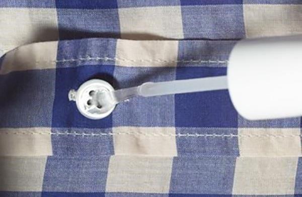 Sewing tip to keep buttons from falling off, a clear nail polish brush touching a button on a blue and cream checked shirt