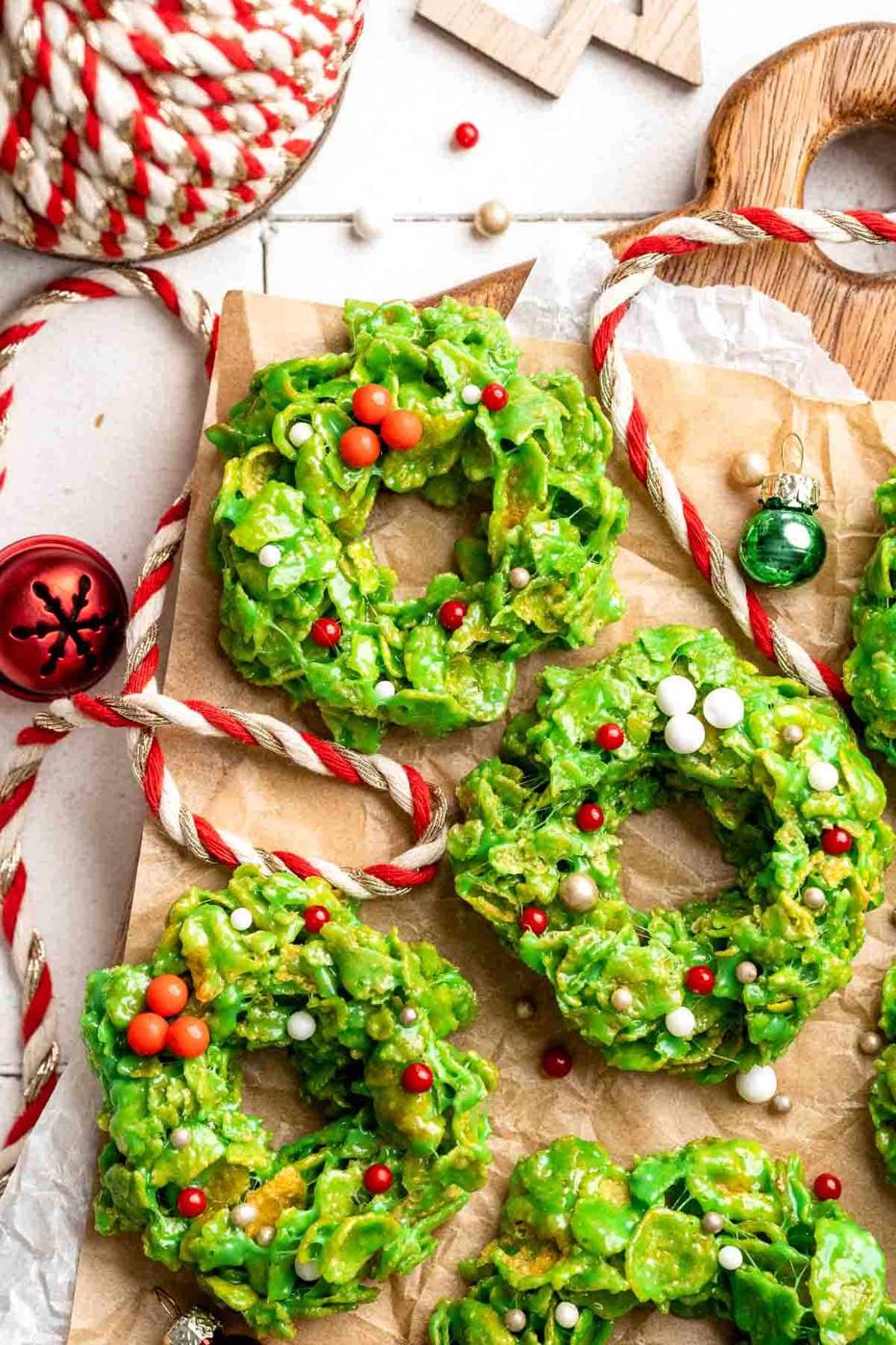 Green cornflake wreath cookies studded with red candy berries and white sprinkles on parchment with red and white twine