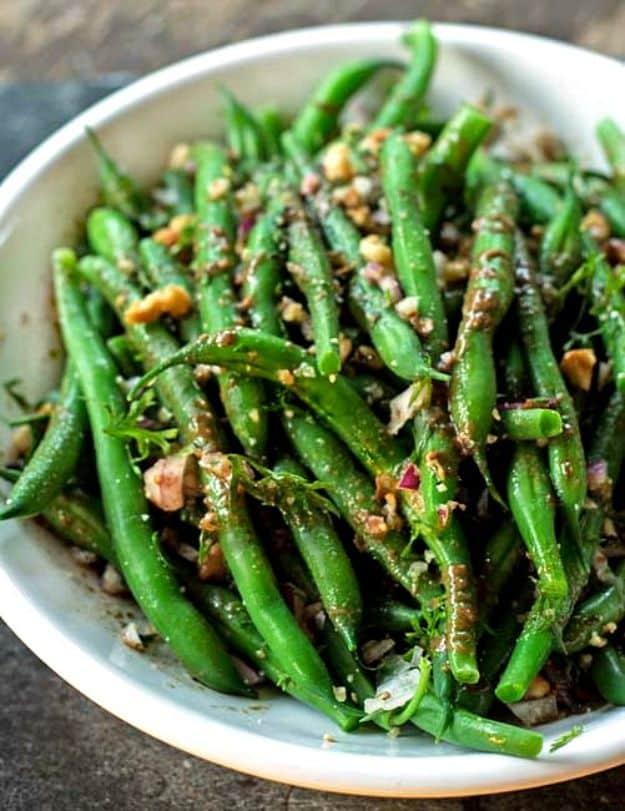 Green bean salad in a shallow bowl with whole green beans, crushed walnuts and chopped red onion on top