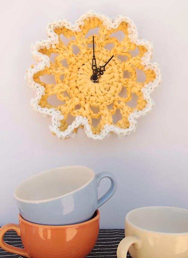 Doily clock crocheted in yellow and cream plastic bag plarn with black clock hands, hung above stacked coffee cups