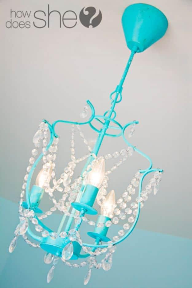 Small turquoise painted chandelier with clear beaded crystal strands, hanging against a plain white wall