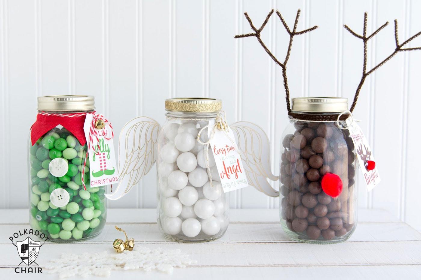 Three Christmas candy mason jars styled as an elf with a red collar, an angel with paper wings and a reindeer with antlers
