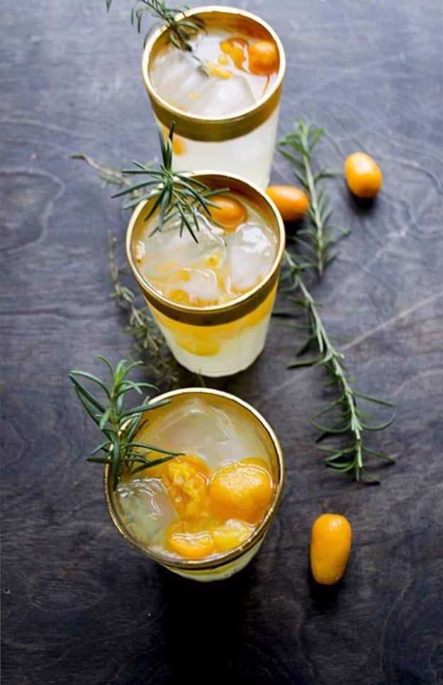 Three tumblers of St. Germain kumquat cocktail over ice with halved kumquats and fresh rosemary sprigs
