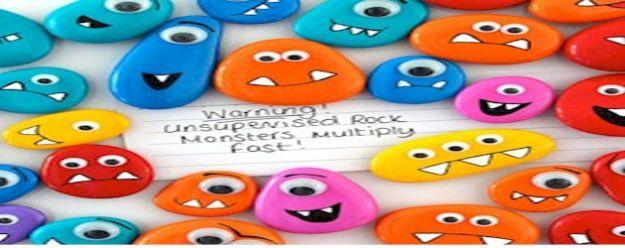 Dozens of pebbles painted as bright monsters with googly eyes and marker mouths, around a handwritten warning card