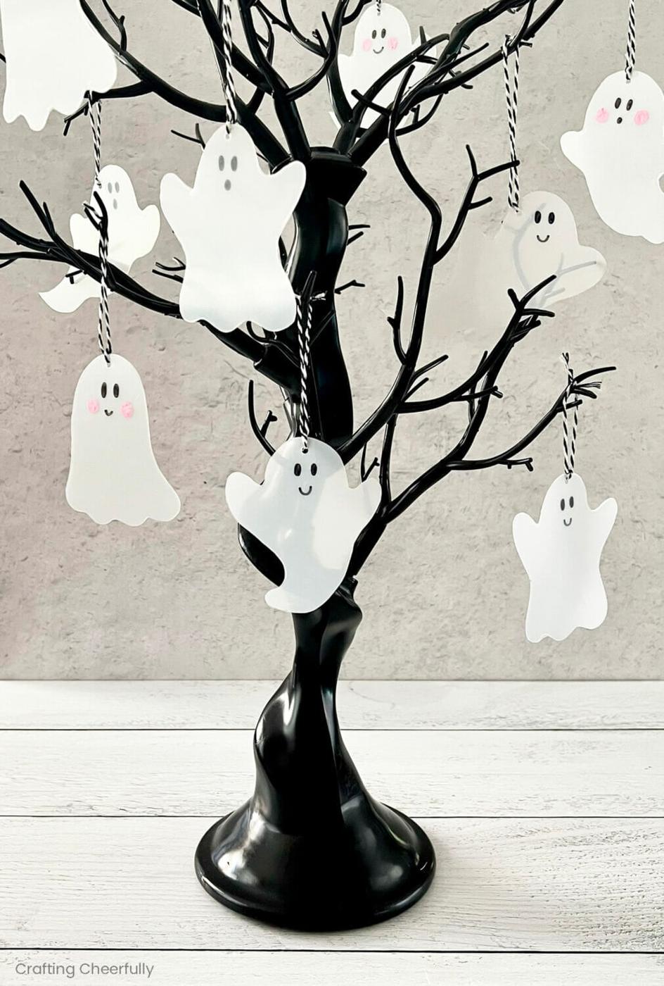 White craft-plastic ghost ornaments with marker faces and twine hangers displayed on a glossy black tabletop tree