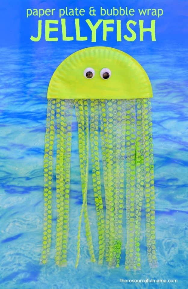 Yellow painted half paper plate jellyfish with long painted bubble wrap tentacles, against a blue water background