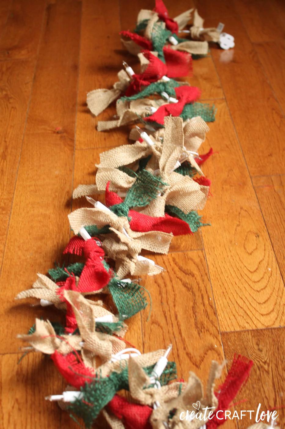 Strand of clear mini lights with short knotted strips of natural red and green burlap covering the wire