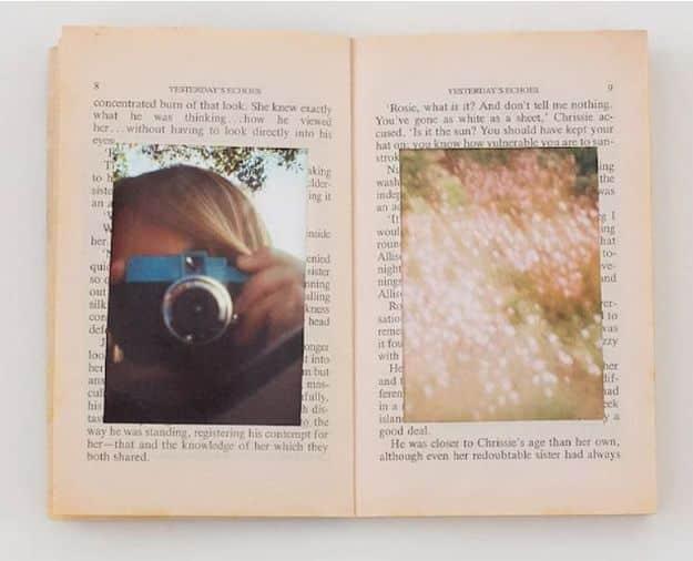 Open vintage hardback book lying flat with two rectangular windows cut through the pages holding photographs