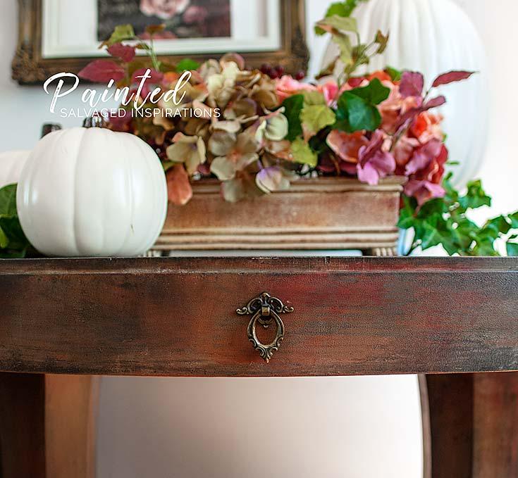 Painted entryway table in layered warm fall tones with a white pumpkin and dried floral arrangement on top