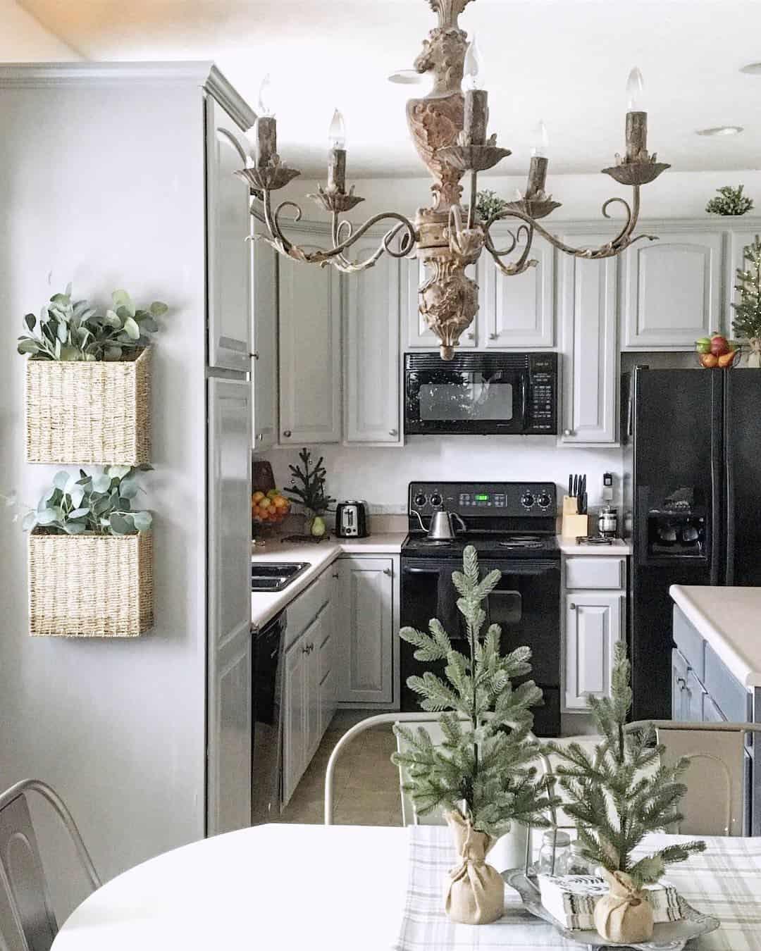 Grey painted kitchen cabinets with an ornate chandelier, black appliances and greenery in woven wall baskets