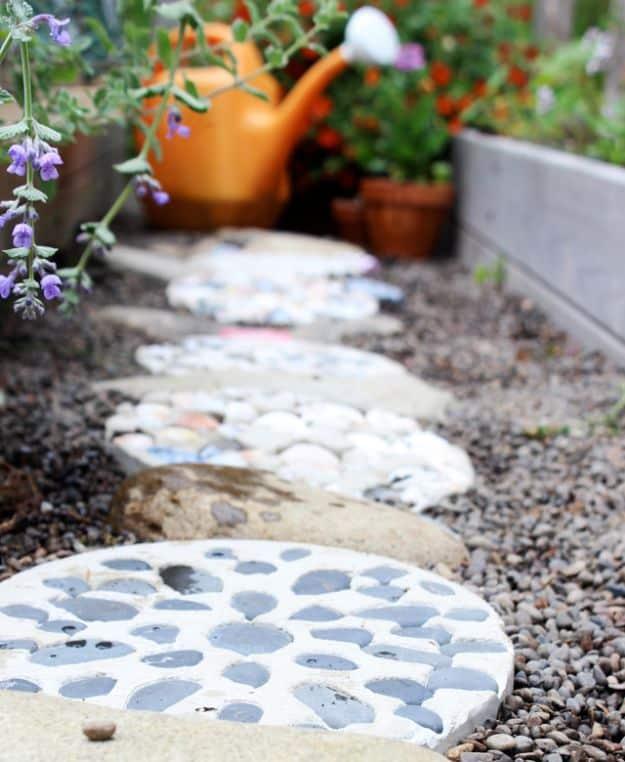 Round cement stepping stones embedded with shells and gray stones set into a gravel bed by a planter