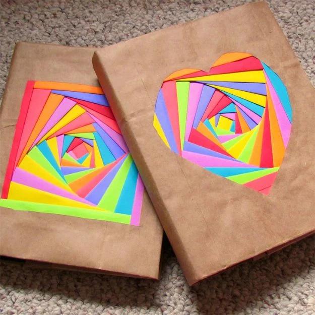 Rainbow iris folded book covers on brown paper grocery bags, one a square spiral and one a heart in bright paper
