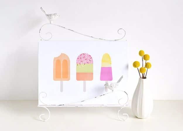 Icy treats printable art, three flat illustrated ice lollies in orange, mint, pink and yellow on a white sheet on a wire