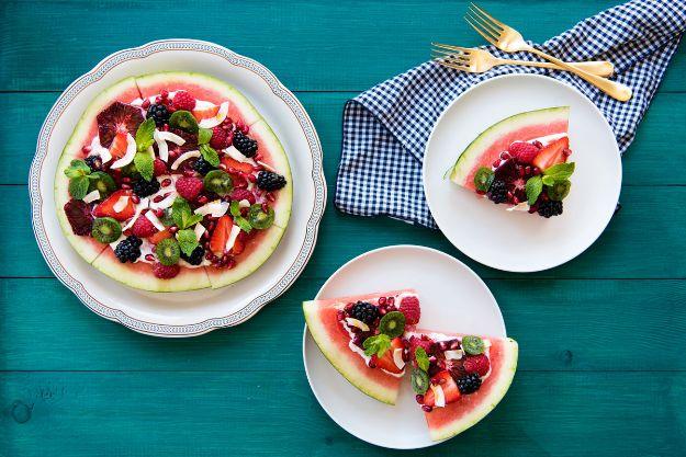 Watermelon pizza rounds spread with yogurt and topped with berries, kiwi and coconut flakes on teal wood