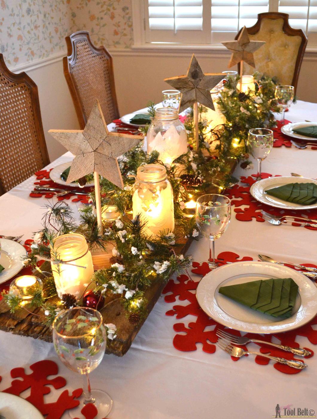 A barn wood board with frosted mason jar candles, wood stars on dowels and snowy garland with fairy lights on a white table