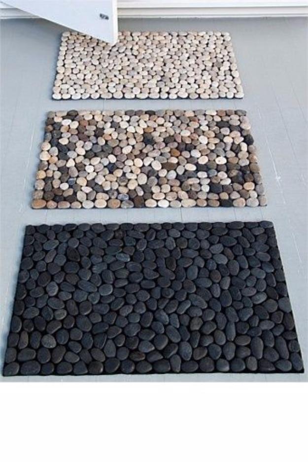 Three pebble bath mats in cream, mixed brown and black river stones, laid one above another on a gray floor