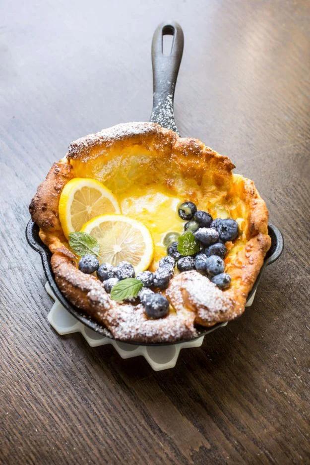 Mini Dutch baby pancakes puffed golden in small skillets, topped with lemon curd and fresh blueberries
