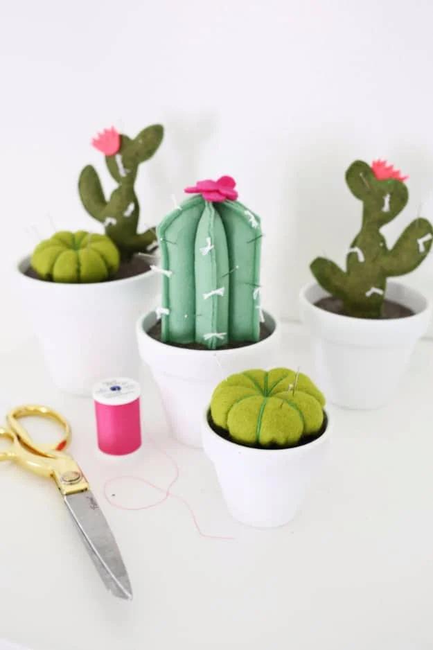 A green felt cactus pin cushion stuck with pins, planted in a tiny terracotta pot on a cluttered sewing table