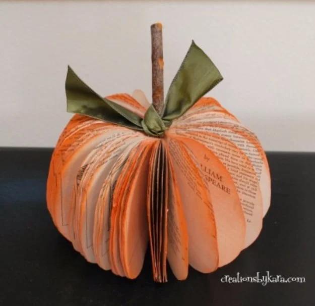 Book page pumpkin made from a cut paperback fanned into a round orange pumpkin with a stick stem and green ribbon