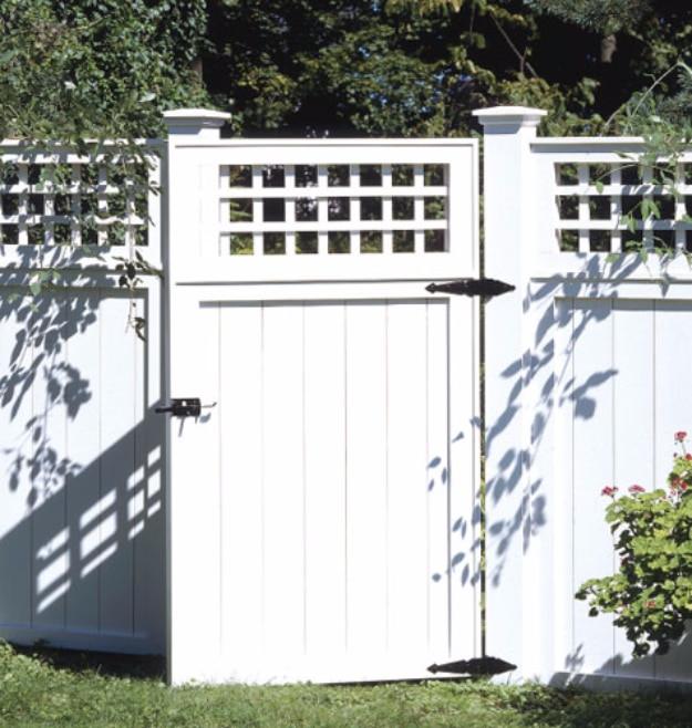 Classic backyard fence, a white painted lattice topped fence and matching gate with black hardware beside flowering shrubs
