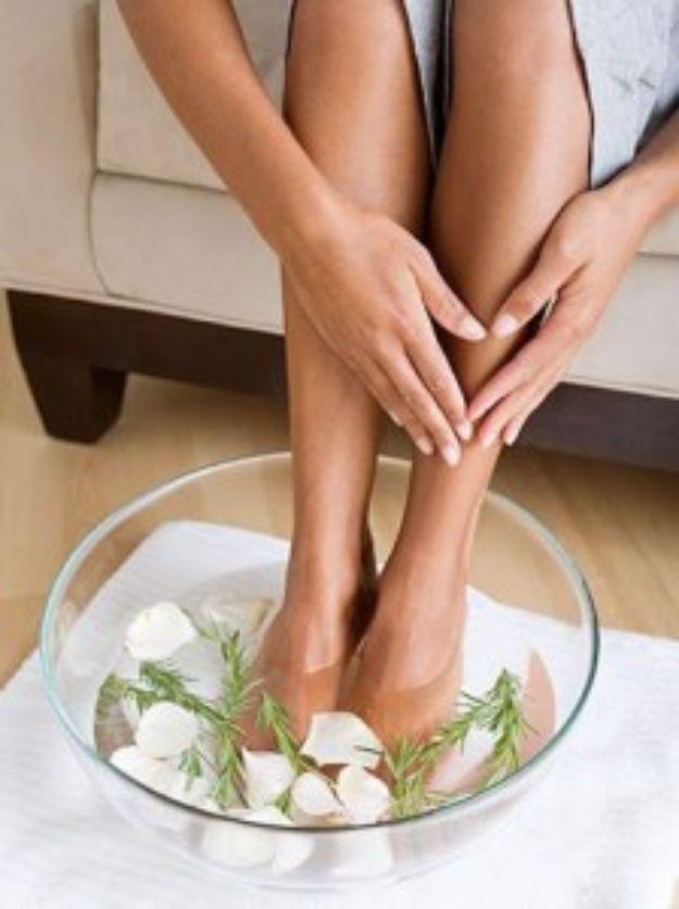 Home spa treatment for dry cracked feet, a woman's feet soaking in a glass bowl of water with rosemary and petals