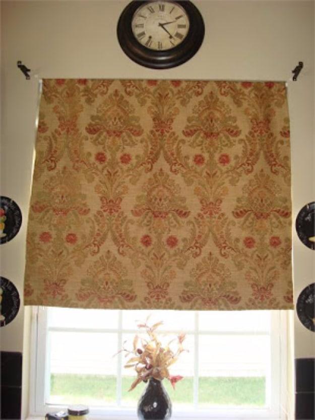 DIY roman shade in gold and red damask fabric gathered into soft folds, hanging below a round wall clock on a cream wall