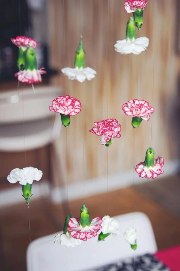 Pink and white carnation heads hanging on invisible strands above a set table in a pale paneled room
