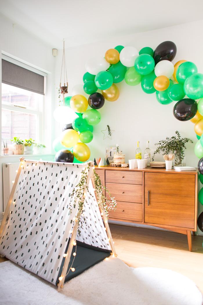 A wooden A-frame play tent with white fabric stamped in black dashes and fairy lights along the edge in a bright living room